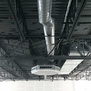 Round exposed ductwork and a ceiling unit under a black steel roof
