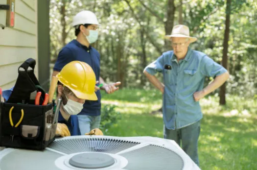 Technicians in hard hats checking an outdoor unit with the homeowner